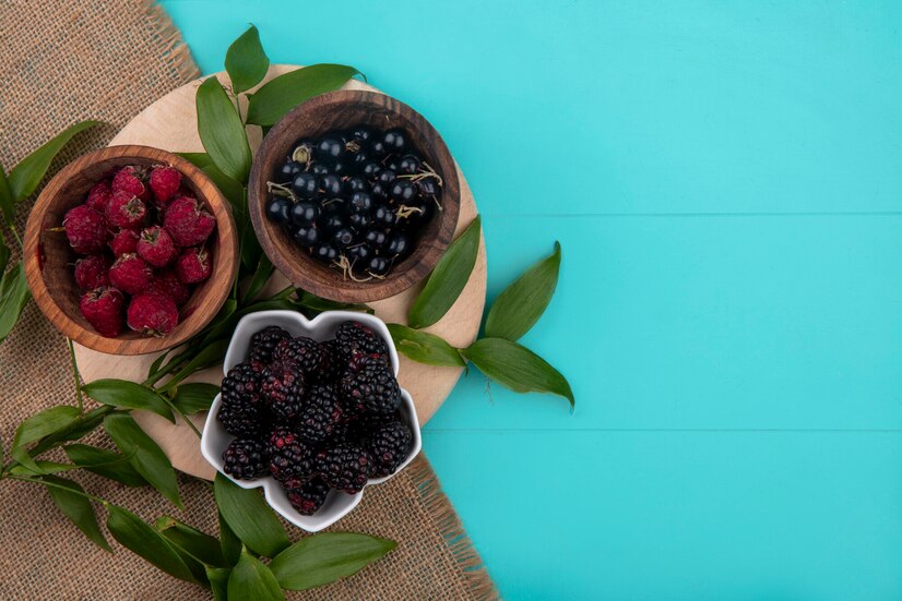 top-view-raspberries-with-black-currants-blackberries-bowls-stand-turquoise-surface_141793-17988