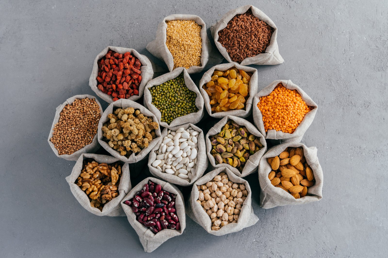 Assorted Grains, Legumes, Nuts and Dried Fruits in Burlap Sacks Arranged on Gray Concrete Surface Assorted Grains, Legumes, Nuts and Dried Fruits in Burlap Sacks Arranged on Gray Concrete Surface