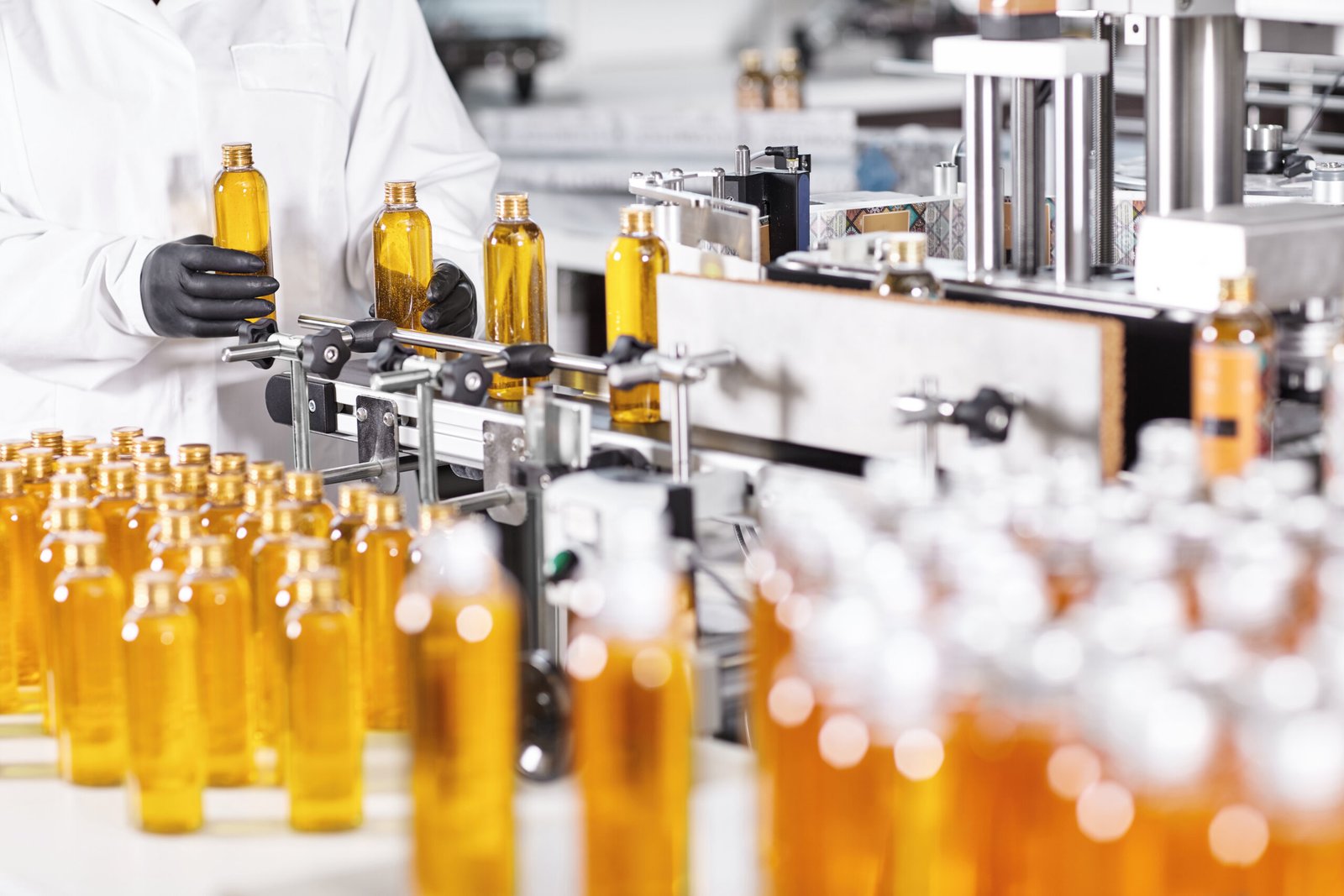 Process of production new type shampoo at factory. Clever young Process of production new type shampoo at factory. Clever young researcher standing near conveyor putting glass bottles at conveyor doing automated work. Production and new technology concept