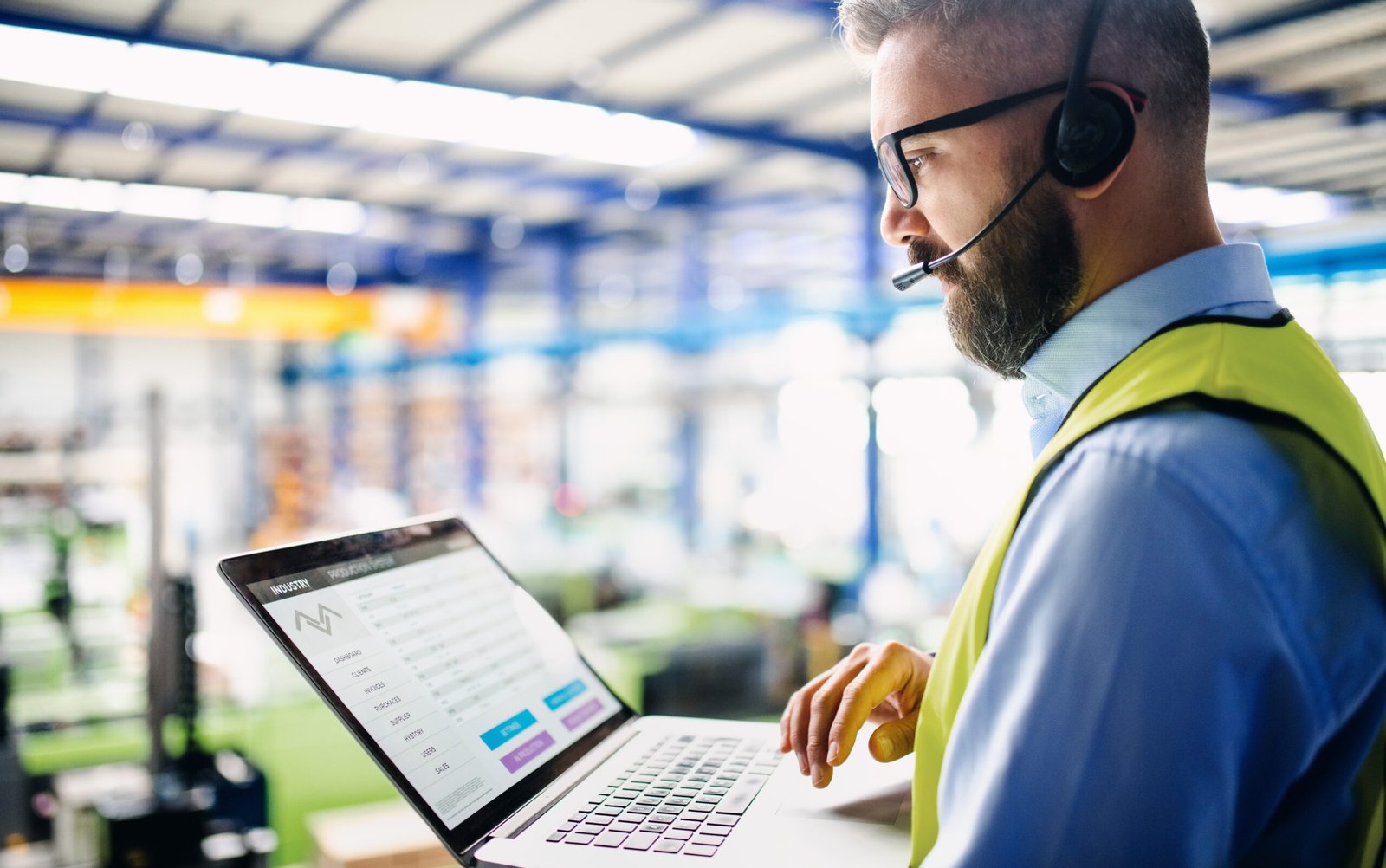 Side view of technician or engineer with headset and laptop standing in industrial factory. Side view of technician or engineer with headset and laptop standing in industrial factory, working.